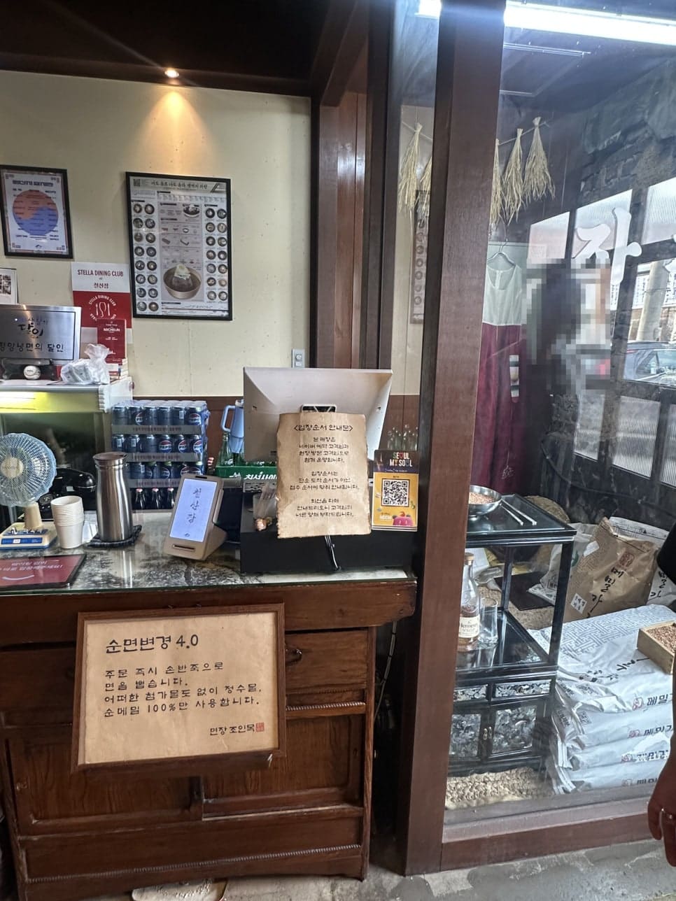 자가제면 안내문 아래 메밀가루 포대가 층층이 쌓여 있고, 처마엔 마른 짚단이 걸려 있습니다.
