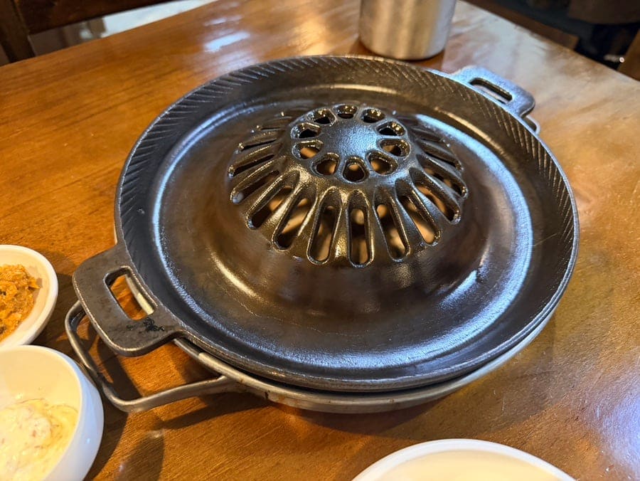 불을 올리기 전 무쇠 불판과, 다 구워 접시에 옮겨 담은 돼지갈비입니다. 두 블로거 모두 이 불판 위에서 육수를 부어가며 굽는 방식을 낯설어했지만,