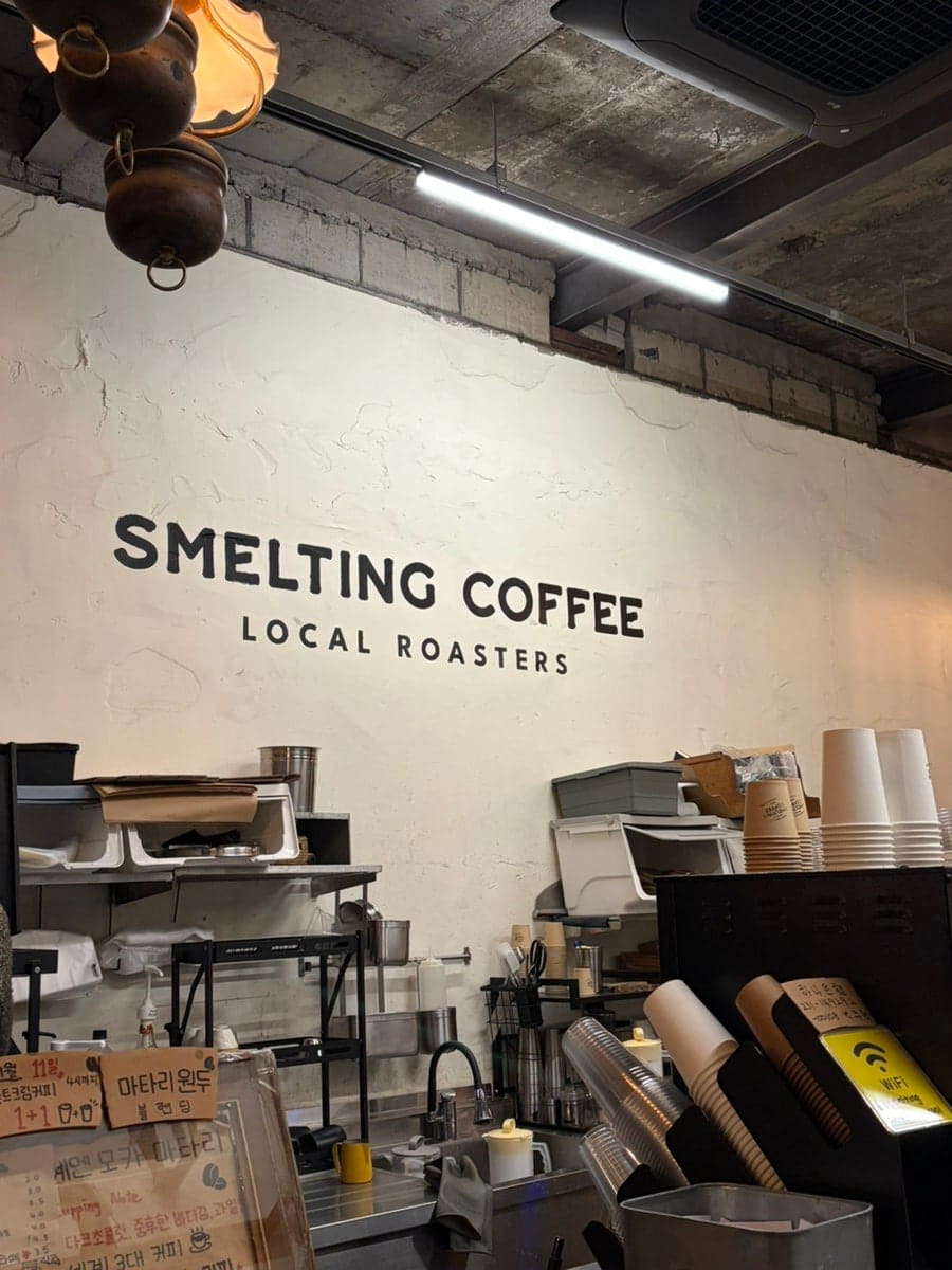 컵 홀더마다 손그림이 그려져 있고, 벽엔 'SMELTING COFFEE LOCAL ROASTERS' 글자가 커다랗게 적혀 있습니다. 평일 오전 여덟 시부터 문을 열고,