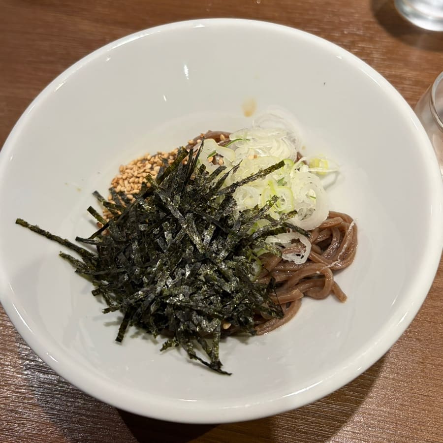 오마카세로 개편된 뒤 데이트로 찾은 손님의 기록입니다. 오픈 주방을 등지고 놓인 사케와, 김가루·참깨·파를 수북이 얹은 들기름 비빔소바가 놓여 있습니다.