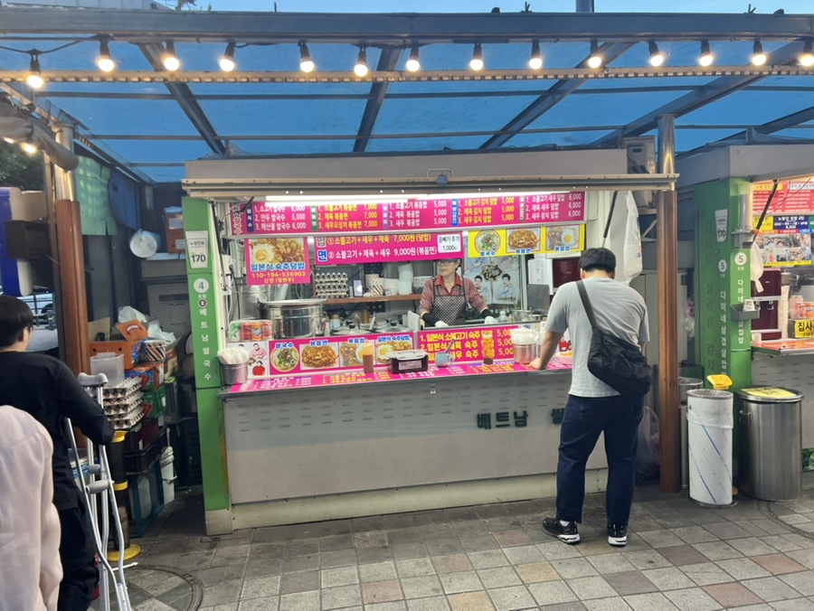 kar7519가 담은 노량진 컵밥거리 입구입니다. 저녁빛 속에 네온 간판이 켜지고, 지붕을 덮은 노점들이 길게 줄지어 있습니다.