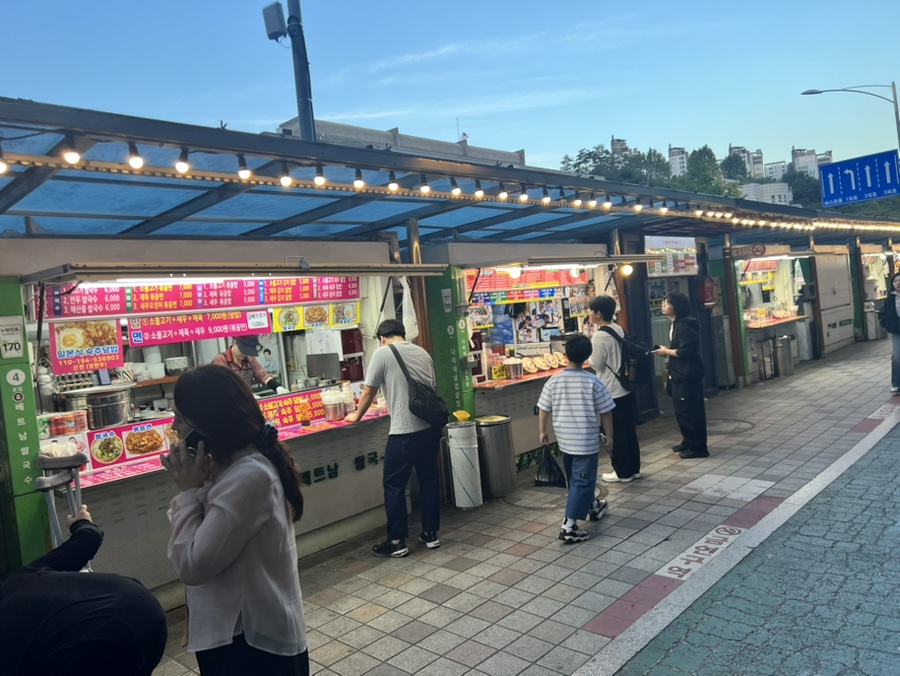 kar7519가 대낮에 담은 장면입니다. 노점 앞에 손님들이 줄지어 서 있고, 왕왕이모네컵밥 가게 안에서는 상인이 쉴 틈 없이 손을 움직입니다.