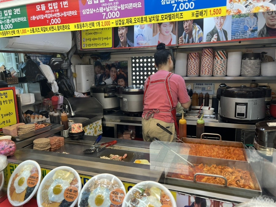 hyunji6370이 다미네에서 담은 사진입니다. 메뉴가 빼곡한 판 아래로, 사장님이 철판 위에서 쉴 틈 없이 음식을 만드는 모습이 보입니다.