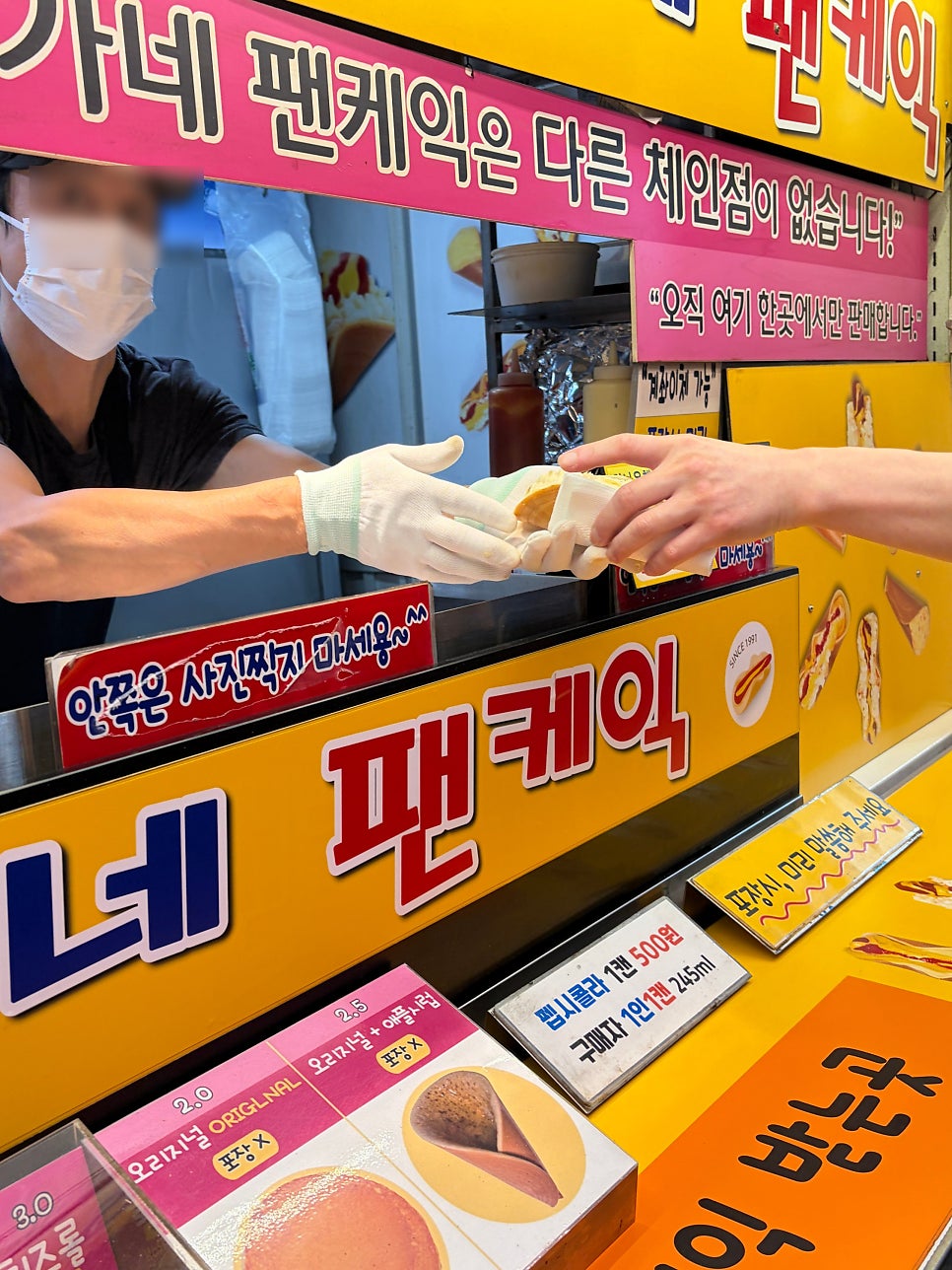 nelphie가 담은 오가네 팬케익입니다. 장갑을 낀 손으로 갓 구운 메뉴를 건네는 순간과, 토마토소스와 치즈가 두툼하게 올라간 완성품을 가까이서 보여줍니다.