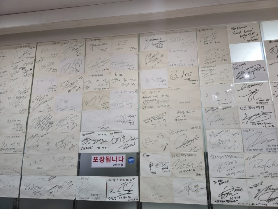 rubung은 가게를 다녀간 손님들이 남긴 사인과 메모가 벽 하나를 빼곡히 채우고 있다고 적었습니다. 사진에는 손님들이 앉아 식사 중인 넓은 홀과,