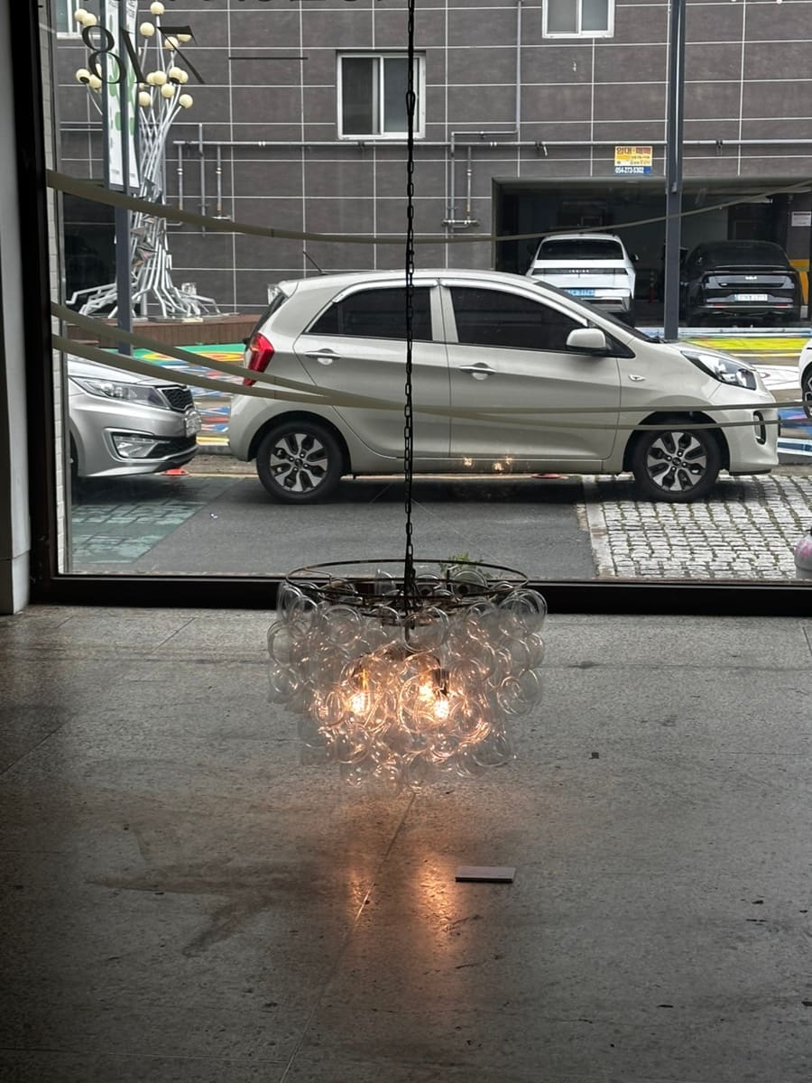 같은 공간 안쪽에서 통유리 너머로 바깥 골목을 담은 사진입니다. 벽화가 그려진 바닥과 주차된 차들이 유리에 비치고,