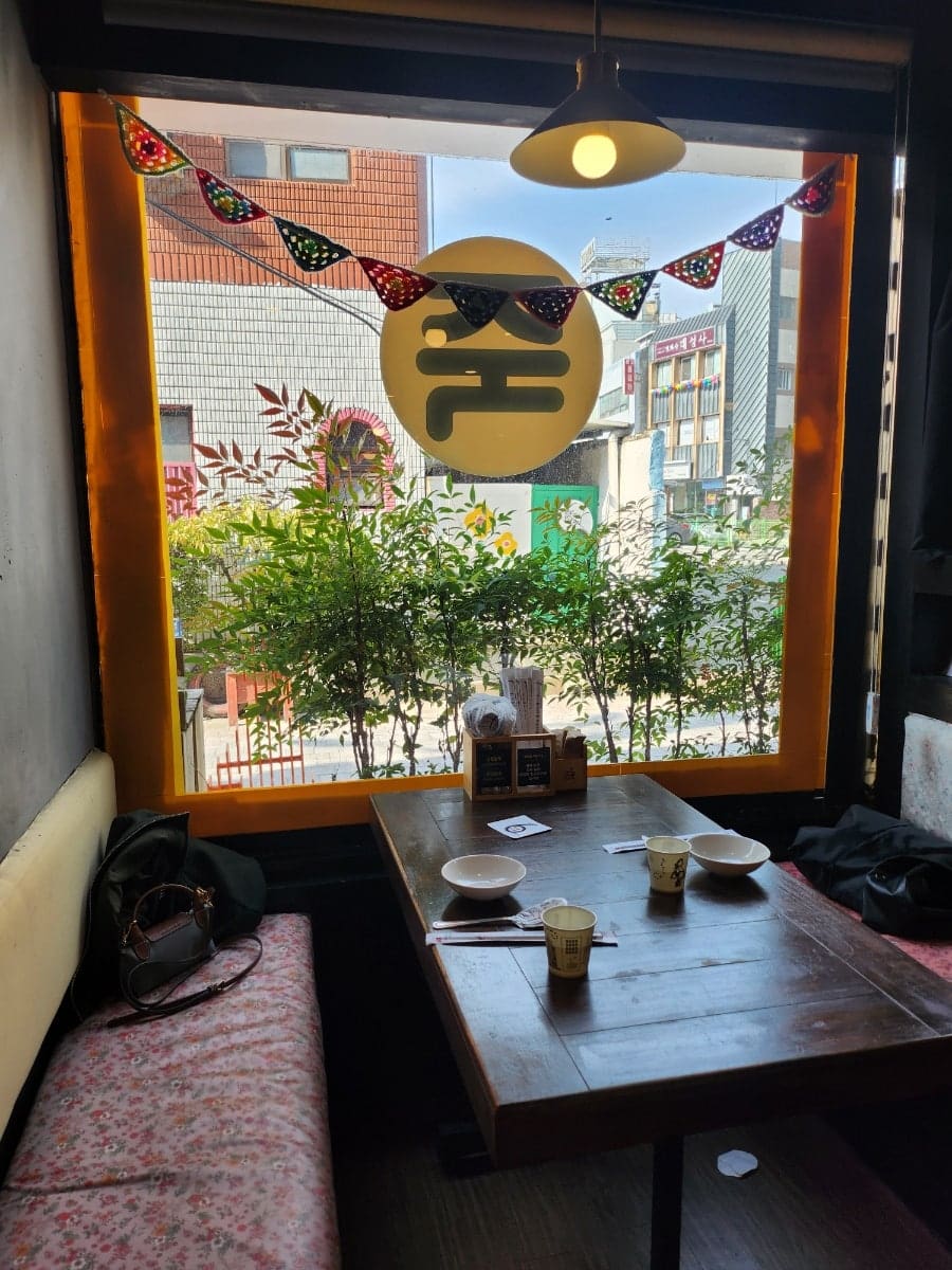 seraphpink가 창가 자리에서 찍은 사진입니다. 주황 테두리 통유리 너머로 바깥 골목이 비치고, 유리에는 가게 이름 한 글자가 커다랗게 그려져 있습니다.