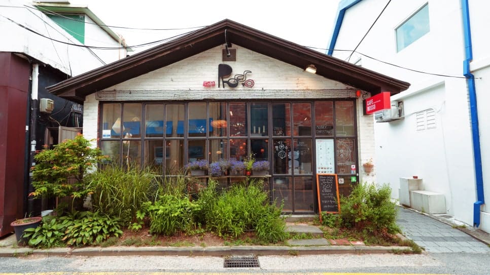 frangdas가 찍은 사진에는 나무 간판에 손으로 새긴 CAFE ROSSO 글자와, 햇살이 비스듬히 들어오는 나무 테이블 위 라떼 한 잔이 담겨 있습니다.