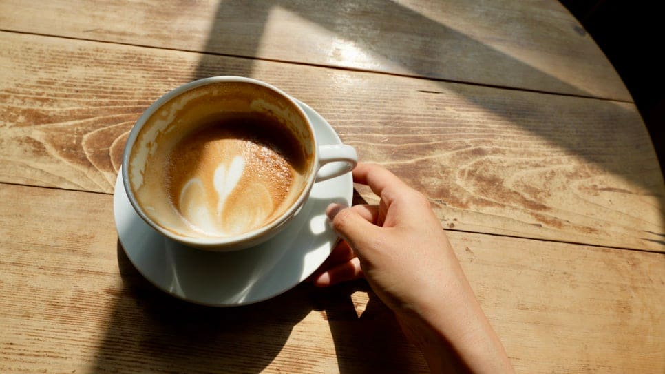frangdas가 찍은 사진에는 나무 간판에 손으로 새긴 CAFE ROSSO 글자와, 햇살이 비스듬히 들어오는 나무 테이블 위 라떼 한 잔이 담겨 있습니다.