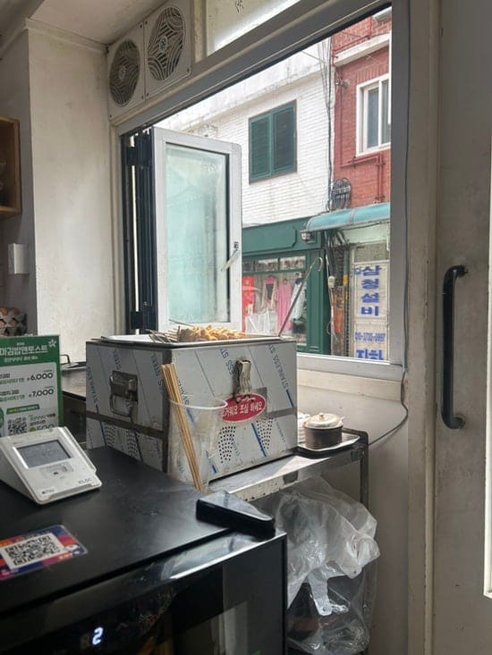 창가 자리에선 토스트 기계 너머로 골목 간판들이 보이고, 다 먹은 자리엔 김밥 접시와 종이컵 두 개가 남아 있습니다. 산책하다 잠깐 들르기 좋은 자리라고 블로거는 적었습니다.