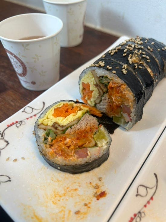 창가 자리에선 토스트 기계 너머로 골목 간판들이 보이고, 다 먹은 자리엔 김밥 접시와 종이컵 두 개가 남아 있습니다. 산책하다 잠깐 들르기 좋은 자리라고 블로거는 적었습니다.