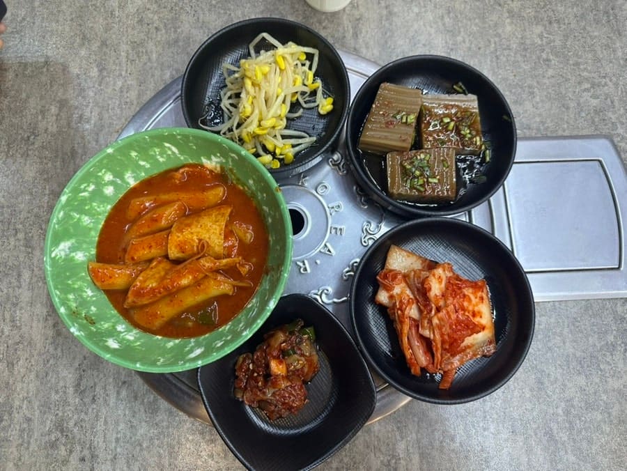이 방문자의 밥상입니다. 콩나물무침, 도토리묵, 김치, 초록 그릇에 담긴 떡볶이까지 다섯 가지 찬이 한 상 가득 올라왔고,