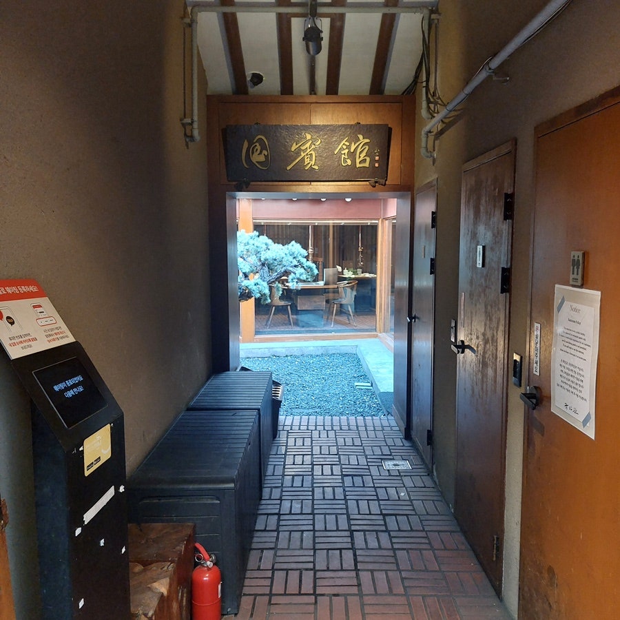 wtwt6767은 '賓館' 현판이 걸린 입구에서 안쪽 마당이 살짝 보이는 복도와, 불판에 불씨가 올라온 바깥 테이블 공간을 담았습니다.