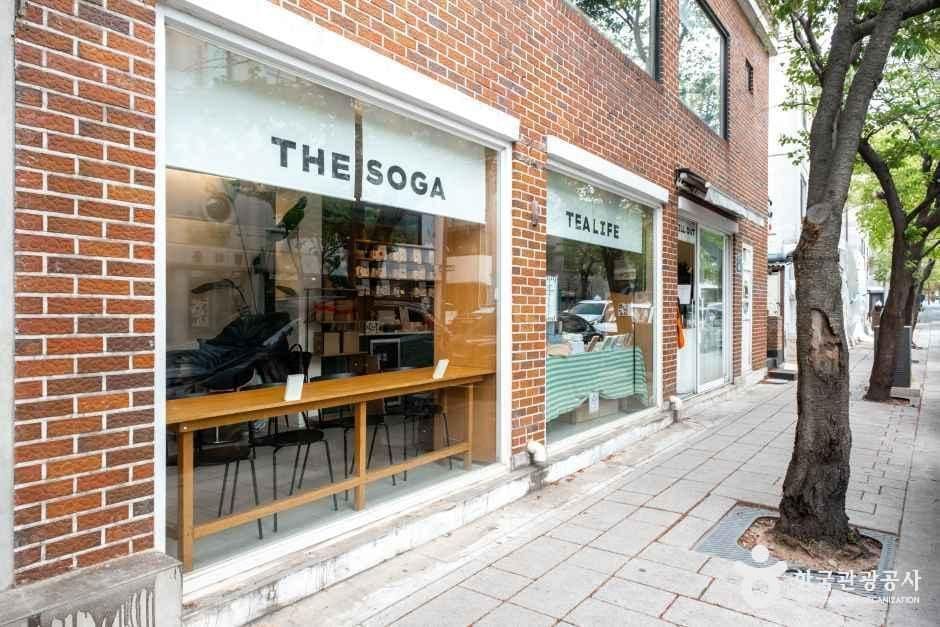 붉은 벽돌 건물에 'THE SOGA'와 'TEALIFE' 간판을 나란히 붙인 가게 외관과, 골목 지붕 너머로 인왕산 바위 능선이 보이는 풍경을 함께 담았습니다.