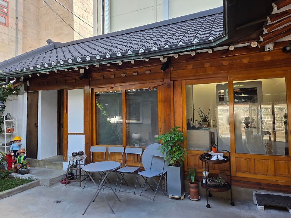 가격표를 옮겨 적어둔 wonderlend82가 찍은 마당과 대문 안쪽입니다. 기와지붕 아래 'COFFEE BAR' 글자가 보이는 마당에 접이식 테이블과 의자가 놓여 있고,