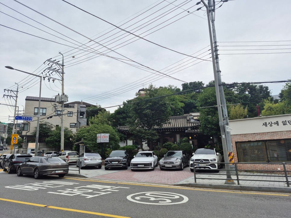 ksana0013이 촬영한 사거리 코너의 노포 '성북동돼지갈비' 건물과, 골목 안쪽 한옥 앞에 나란히 주차된 외제 세단들입니다.
