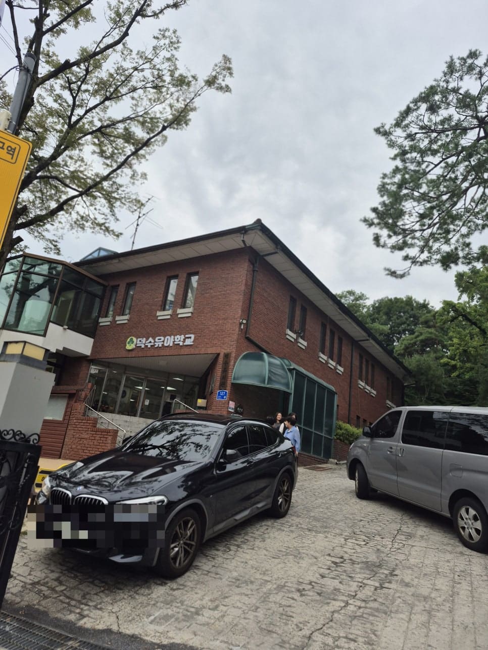 ksana0013이 촬영한 오르막길의 덕수유치원 건물과, 그 위쪽 새로 지어진 카페 건물 앞에 줄지어 주차된 차량들입니다.
