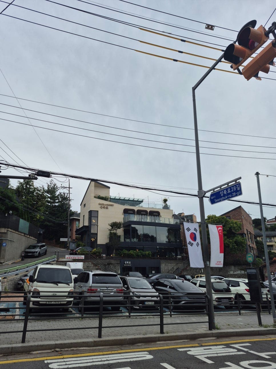 ksana0013이 촬영한 오르막길의 덕수유치원 건물과, 그 위쪽 새로 지어진 카페 건물 앞에 줄지어 주차된 차량들입니다.