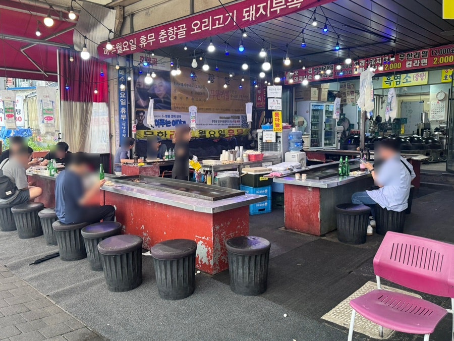 dodolzz가 촬영한 춘향골 외관입니다. 매주 월요일 휴무, 오리고기·돼지부속 무한리필이라고 적힌 현수막 아래로 드럼통 의자가 줄지어 놓여 있고,