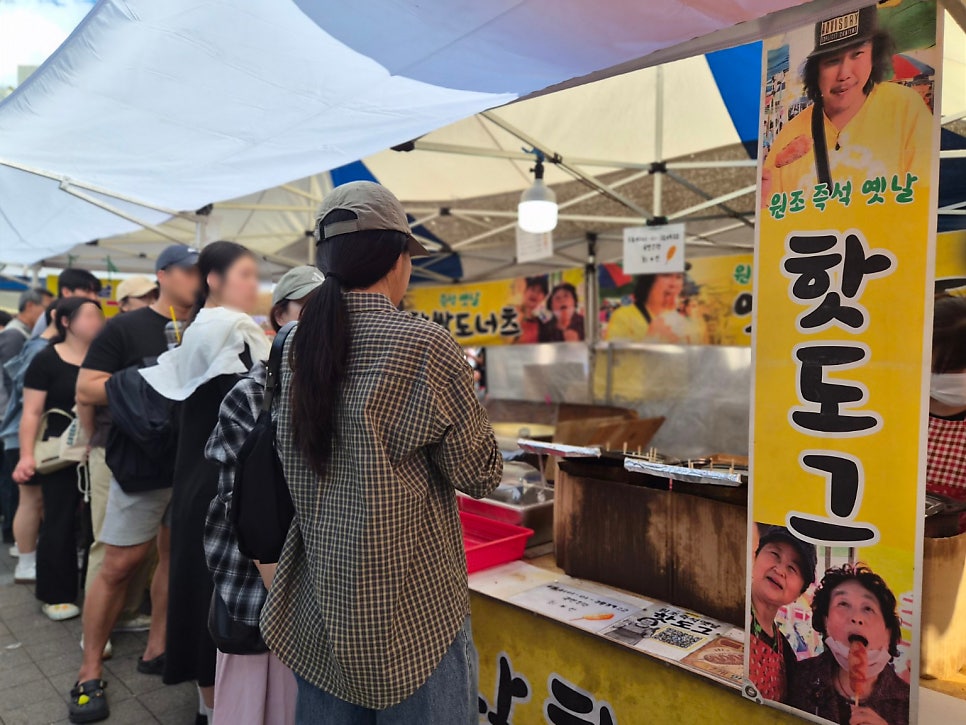 bugtvkr가 찍은 모란시장 입구와 핫도그 노점입니다. 버섯 모양 지붕 아래 장날 인파가 오가고, 다른 한편에서는 줄을 선 사람들이 핫도그를 기다립니다.