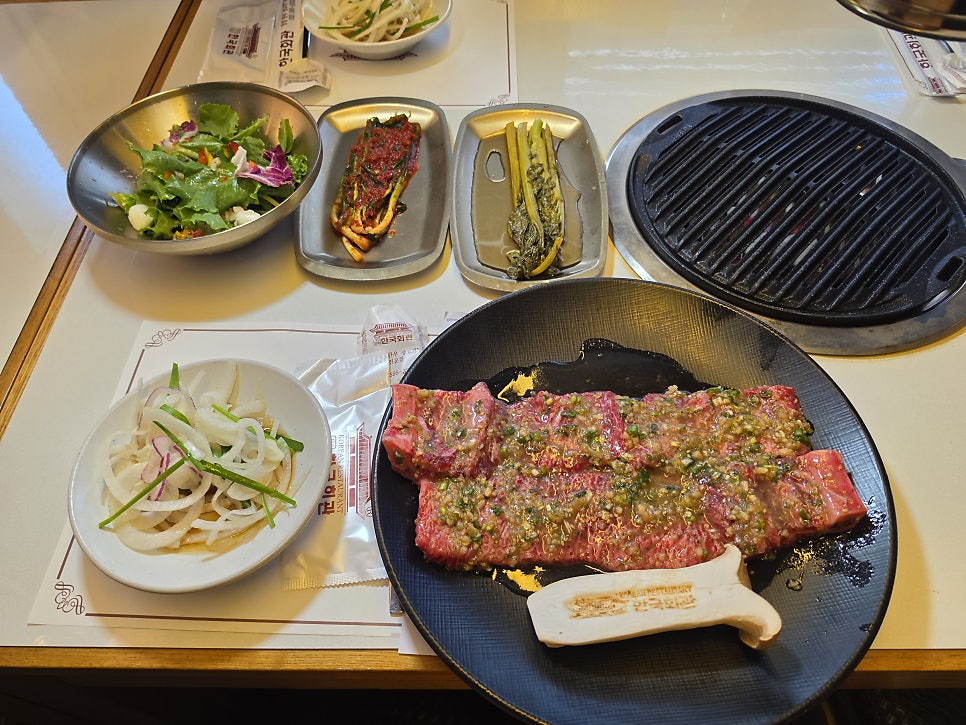 같은 분이 고기가 올라가기 직전에 찍은 사진입니다. 다진 마늘과 쪽파 양념이 듬뿍 올라간 생갈비가 불판 옆 검은 접시에 놓여 있고,
