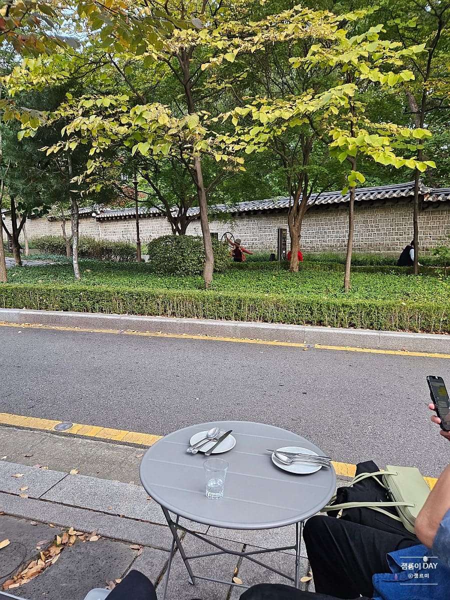 jammm2_는 야장 테이블에 자리 잡고 와인을 즐기고 왔다고 적었습니다. 첫 사진에는 회색 원형 테이블 너머로 도로와 가로수, 기와를 얹은 돌담이 이어지는 풍경이 담겼고,