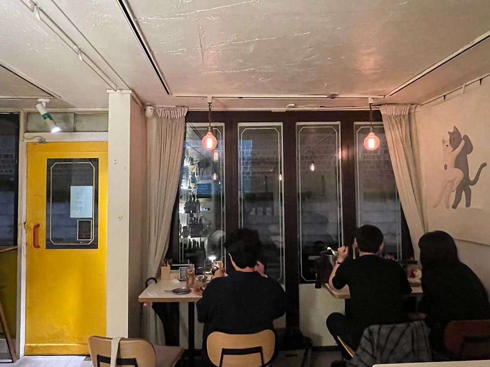 ssonoim은 성벽을 바라보며 먹는 분위기가 참 좋았다고 적었습니다. 첫 사진은 비 오는 밤 커튼을 걷은 창 너머로 조명이 켜진 돌담이 비치는 실내 풍경이고,