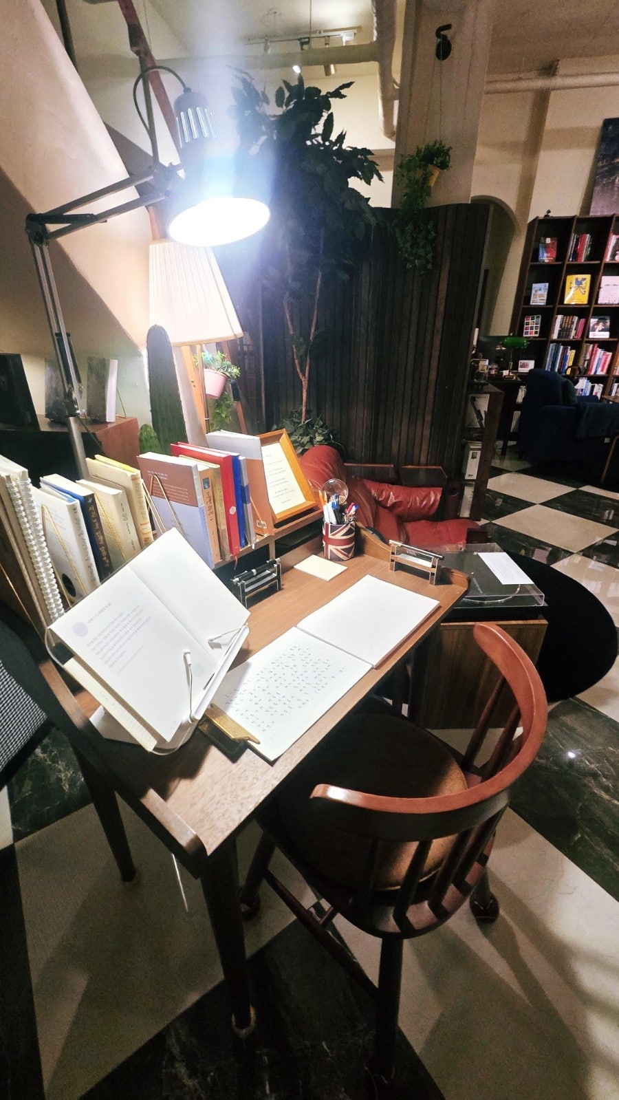 cafebookpang은 스탠드 조명 아래 혼자 앉아 쓸 수 있는 책상과, 벽을 가득 채운 책장이 있는 큰 테이블을 담았습니다.