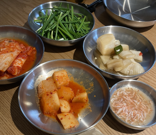 lucky_milk26은 나무 대들보 아래 직원들이 솥 앞에서 조리하는 모습과, 상에 먼저 나온 기본찬을 함께 담았습니다.