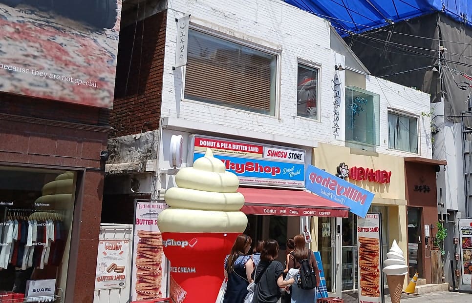 namsikc가 성수동 카페거리를 걸으며 남긴 사진입니다. 오래된 건물 1층에 들어선 디저트 가게 간판과 그 앞에 늘어선 줄이 눈에 띕니다.