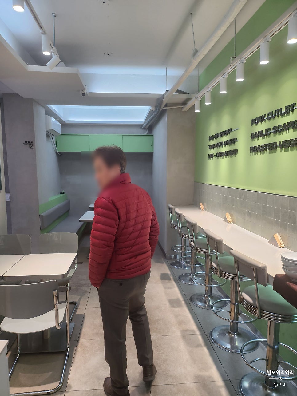 870228j가 찍은 매장 안쪽 바 테이블입니다. 스테인리스 스툴이 나란히 놓여 있고, 뒤쪽 벽에는 메뉴를 설명하는 영문 문구가 큼직하게 붙어 있습니다.