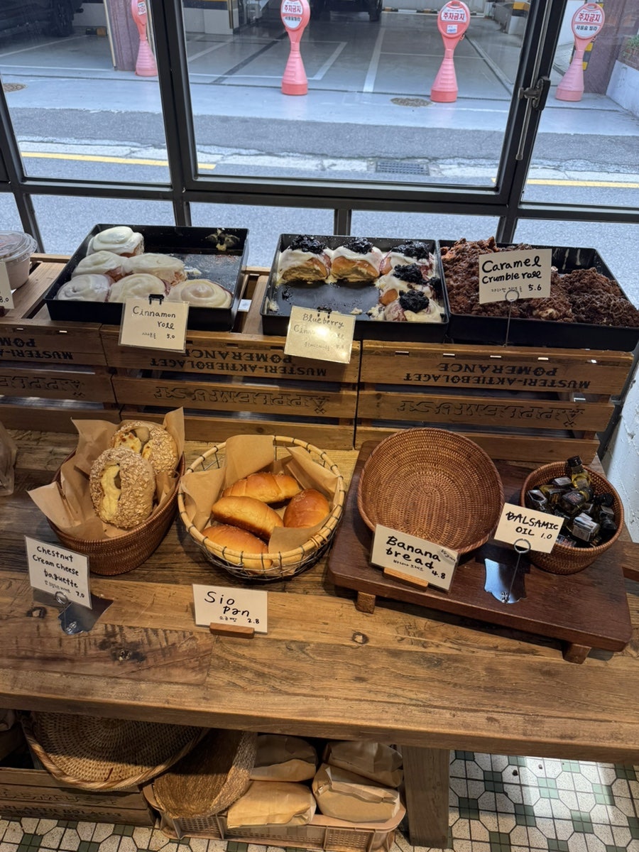 choieun10이 찍은 창가 진열대입니다. 시나몬롤과 블루베리 시나몬롤, 캐러멜 크럼블 롤이 나란히 놓여 있고, 창 너머로는 거리 풍경과 주차금지 표지판이 비칩니다.