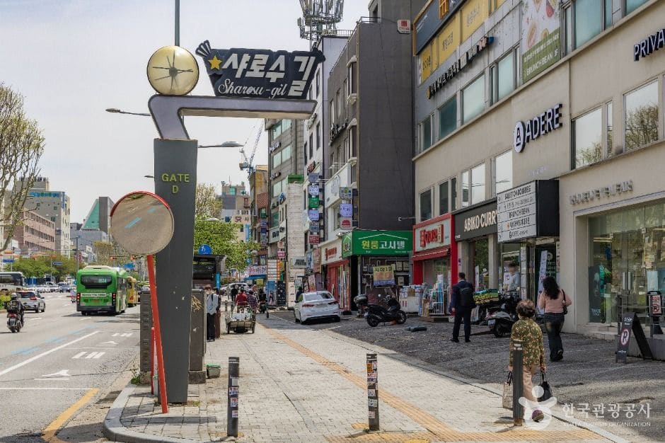별 모양 장식이 달린 '샤로수길 Sharosu-gil' 입간판을 두 각도에서 담았습니다. 한쪽은 버스와 노점이 지나는 큰길 쪽이고,