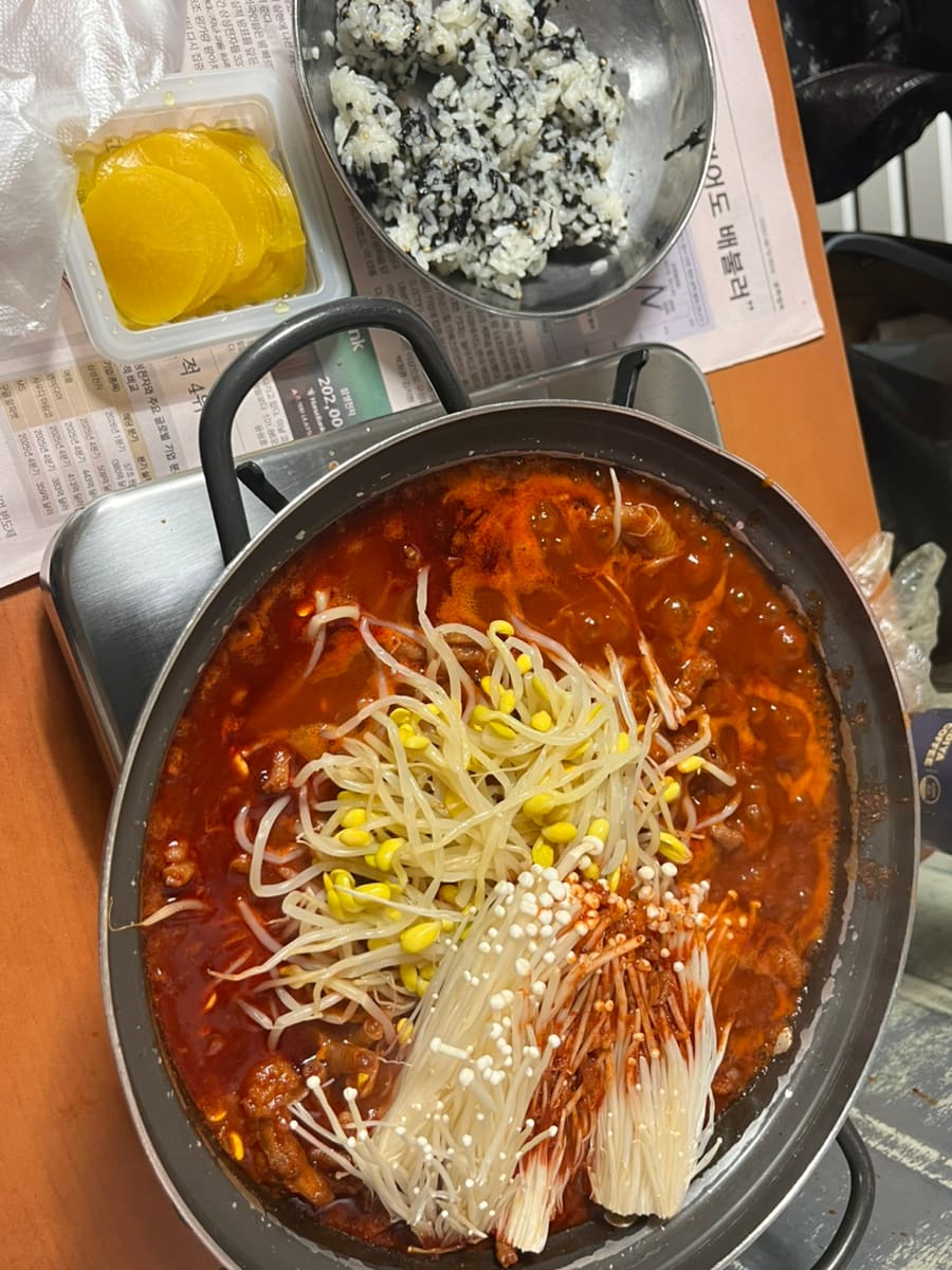 매콤한 국물에 콩나물과 팽이버섯을 얹은 닭발 전골이 불판 위에서 보글보글 끓고 있습니다. 노란무와 주먹밥까지 곁들인 한 상 차림을 블로거는 그대로 담았습니다.