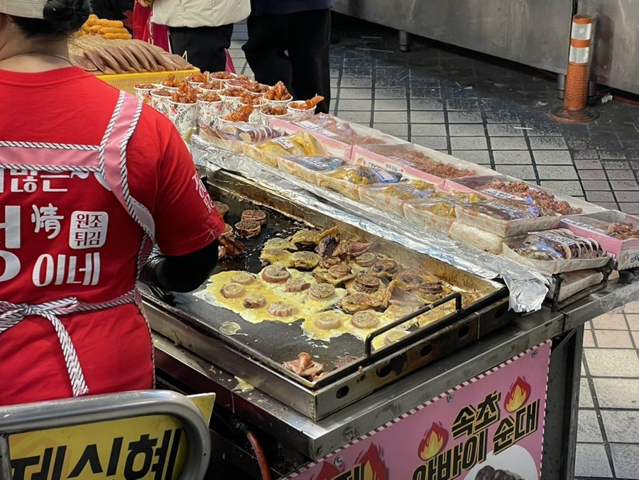 rnjsalsdudd가 찍은 직원 뒤편 앞치마에는 '정이네' 글자가 크게 박혀 있고, 철판 위에서는 오징어순대 단면이 노릇하게 구워지고 있습니다.