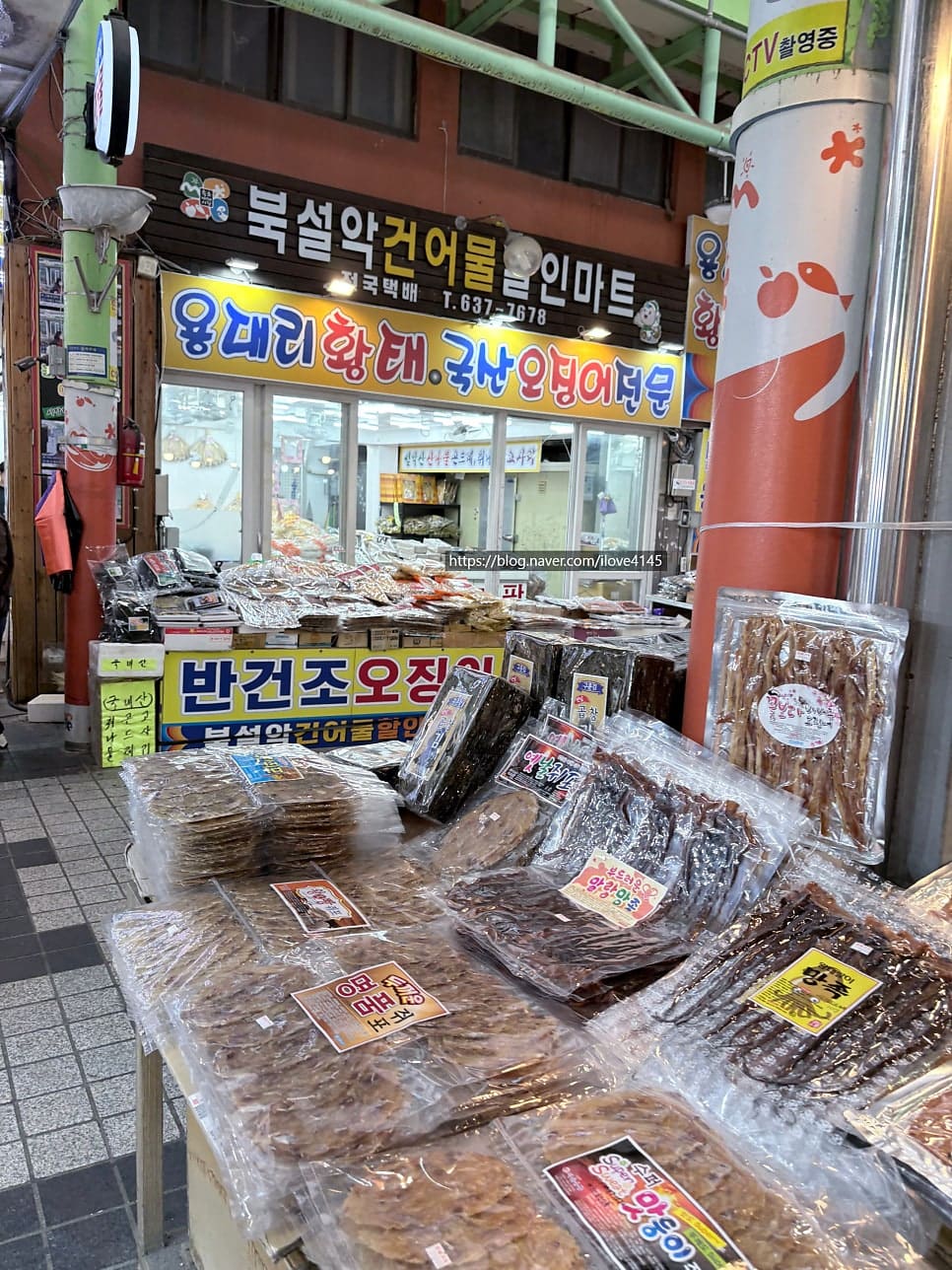 ilove4145가 찍은 건어물 가게 앞에는 반건조 오징어와 황태가 좌판 가득 펼쳐져 있습니다. 같은 블로거가 돌아서서 찍은 통로에는 사람들이 길게 줄지어 걷고 있습니다.