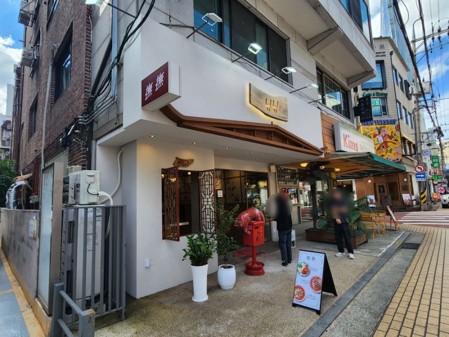 herutopia가 촬영한 송리단길 초입 거리 풍경입니다. 롯데타워가 멀리 보이는 이 대로변에서 상가 간판이 빼곡히 늘어선 골목의 규모를 짐작할 수 있습니다.