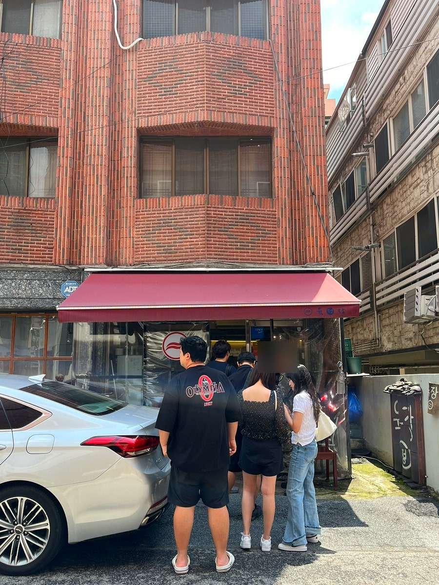 dpwls8332가 담은 기와 간판과 웨이팅 줄입니다. 깨진 기와 조각을 쌓은 담장에 상호를 적은 작은 패가 매달려 있고, 점심시간 가게 앞으로 손님들이 줄을 서 있습니다.