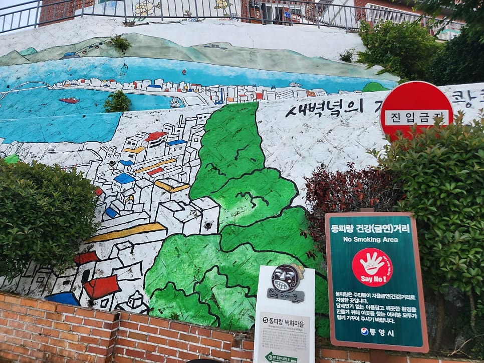 provence_pension이 이른 아침에 남긴 사진입니다. 산허리에 안개가 낮게 걸린 통영 시내 전경과, 골목 입구의 벽화·안내판을 담았는데,