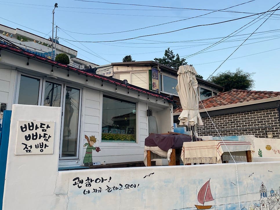 kms920000이 남긴 사진입니다. '빠담빠담 점빵' 손글씨 간판과 캐릭터 벽화, 그리고 필름 모양 안내판이 걸린 목조 담장 전경을 담았는데,