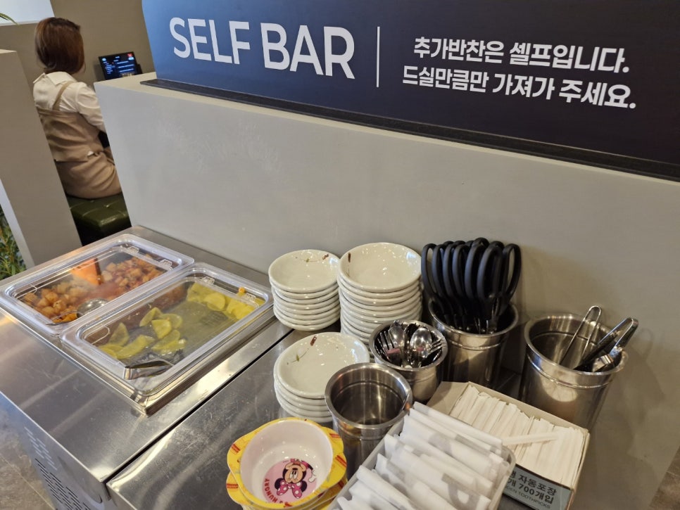 ufkrc8756이 남긴 사진입니다. 셀프 코너에 놓인 반찬과 그릇, 수저통을 담았습니다. 사이드 반찬은 셀프 코너에서 필요한 만큼 가져다 먹는 방식이었다고 적었습니다.