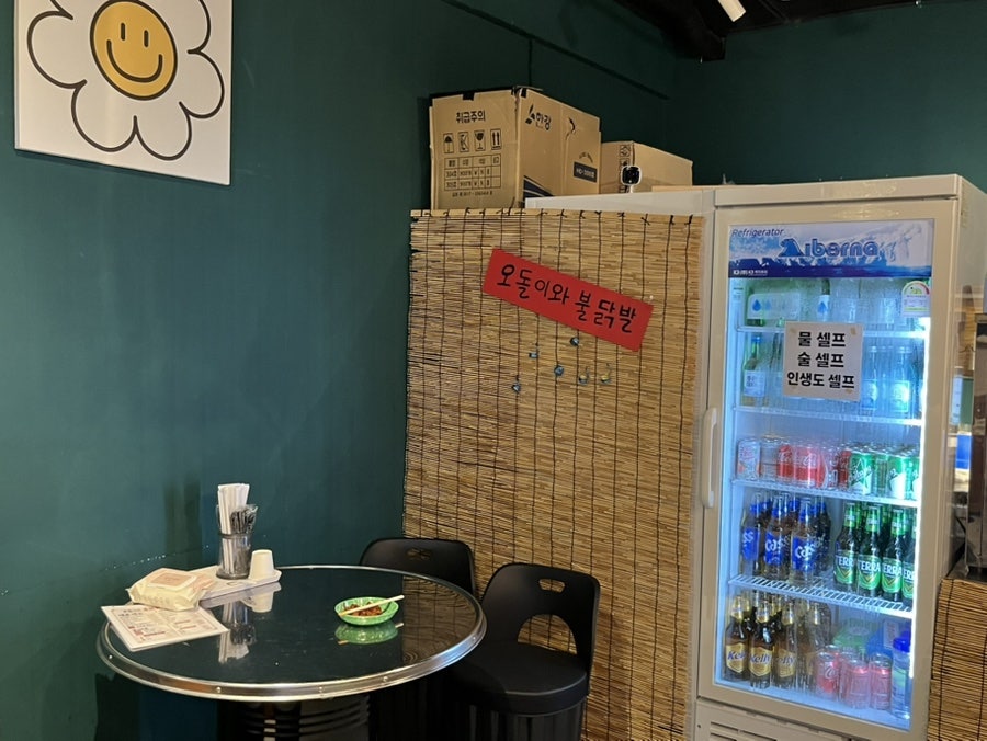 zzeyeon_이 남긴 사진입니다. 꽃 포스터와 손글씨 간판이 붙은 대나무 발 옆으로 음료 냉장고가 놓인 구석 자리를 담았습니다. 물과 술은 셀프였고,
