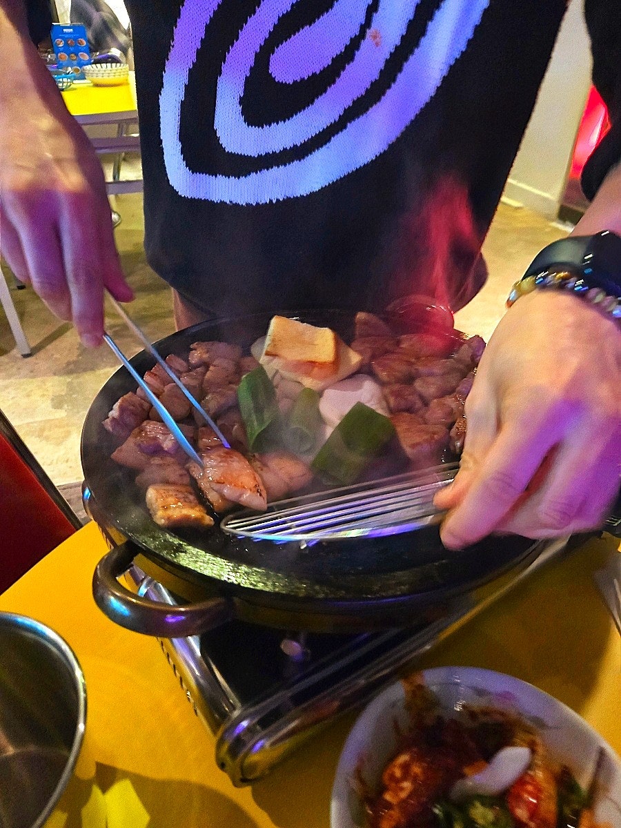 mini123_은 고기를 테이블에서 직접 구울지 주방에서 받을지 고를 수 있다고 적었습니다. 사진에는 불길이 오르는 돌판 위로 집게를 든 손이 고기를 뒤집는 장면과,