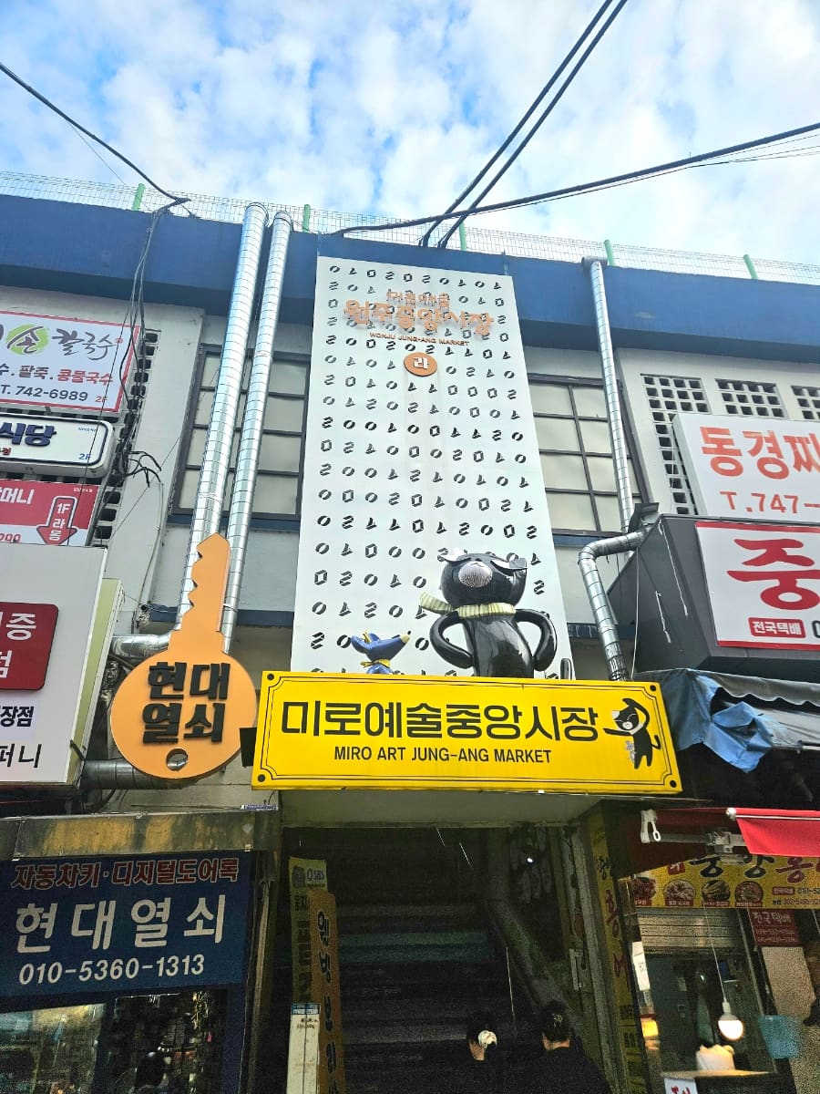 원주중앙시장 2층 입구에 들어서면 '미로예술(원주중앙시장)' 버스 정류장 표지판과 순찰모를 쓴 까만 고양이 마스코트 조형물이 먼저 손님을 맞는다고 konari33은 적었다.