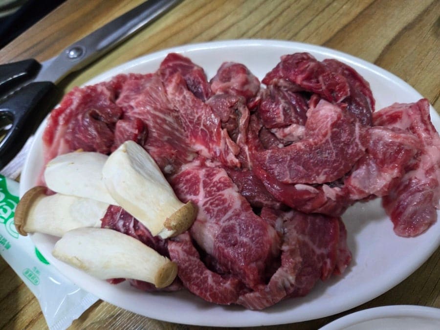 hoitreasure가 주문 직후와 굽는 과정을 함께 남겼습니다. 새송이버섯과 함께 담긴 선홍빛 생고기 접시, 그리고 숯불 석쇠 위에서 지글지글 구워지는 고기 사진입니다.
