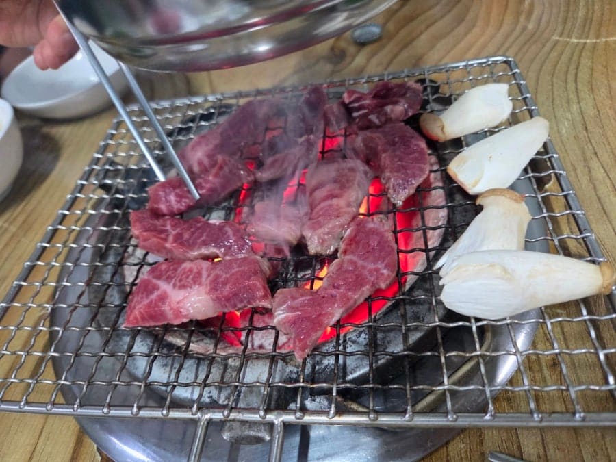 hoitreasure가 주문 직후와 굽는 과정을 함께 남겼습니다. 새송이버섯과 함께 담긴 선홍빛 생고기 접시, 그리고 숯불 석쇠 위에서 지글지글 구워지는 고기 사진입니다.