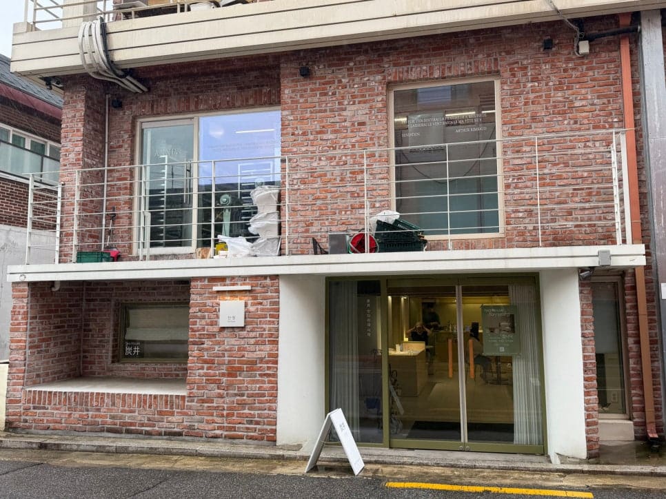 연희동 골목의 붉은 벽돌 건물, 티하우스 탄정의 외관입니다. 통유리 너머로 손님을 맞는 실내가 보이고, 안쪽 다관과 찻잔이 놓인 조리대에서는 차를 우릴 준비가 한창입니다.