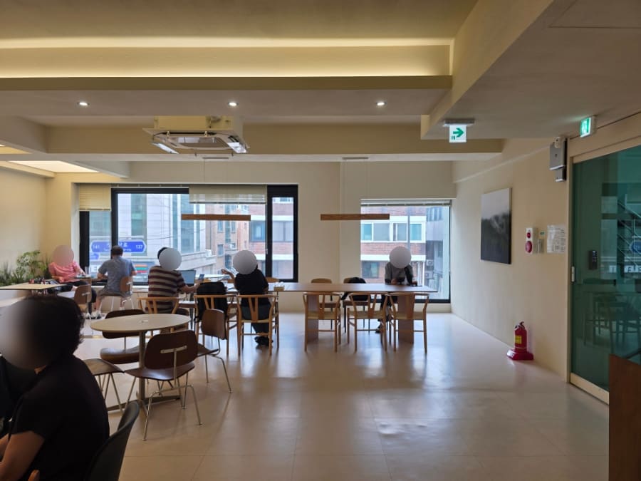 미니멀한 원목 식탁과 창밖 붉은 벽돌 건물, 그리고 인도에 세워둔 'CAFE' 입간판입니다. 커피와 티,