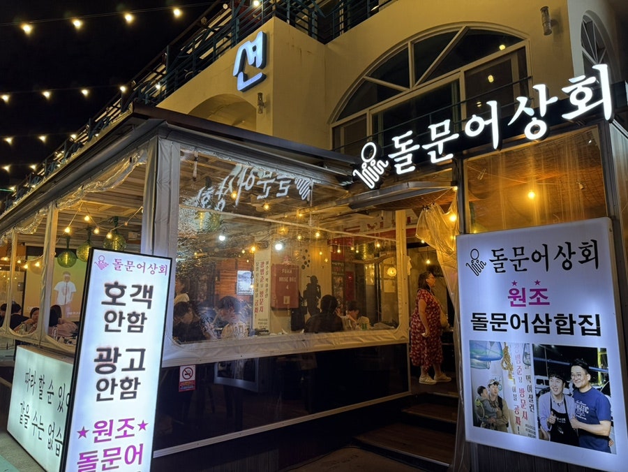 boboworld85가 담은 밤의 외관입니다. '여수를 먹여살린 장범준님이 2번 방문한집'이라 적힌 띠배너 아래로 '돌문어상회' 간판이 환하게 켜져 있고,