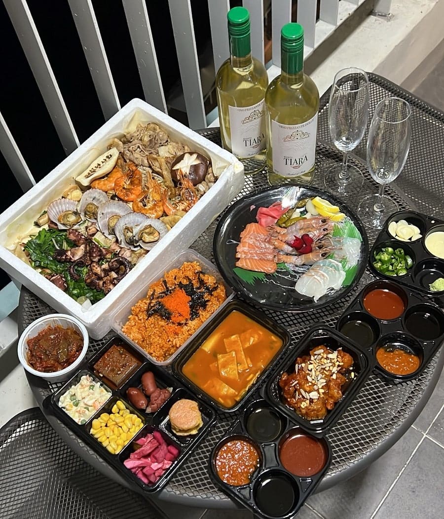 megnon456이 남긴 포장 상차림입니다. 장군님세트를 포장해 숙소 테라스로 가져와 화이트와인과 함께 차려 두었고, 사시미와 딱새우, 해물모듬까지 한 상 가득입니다.